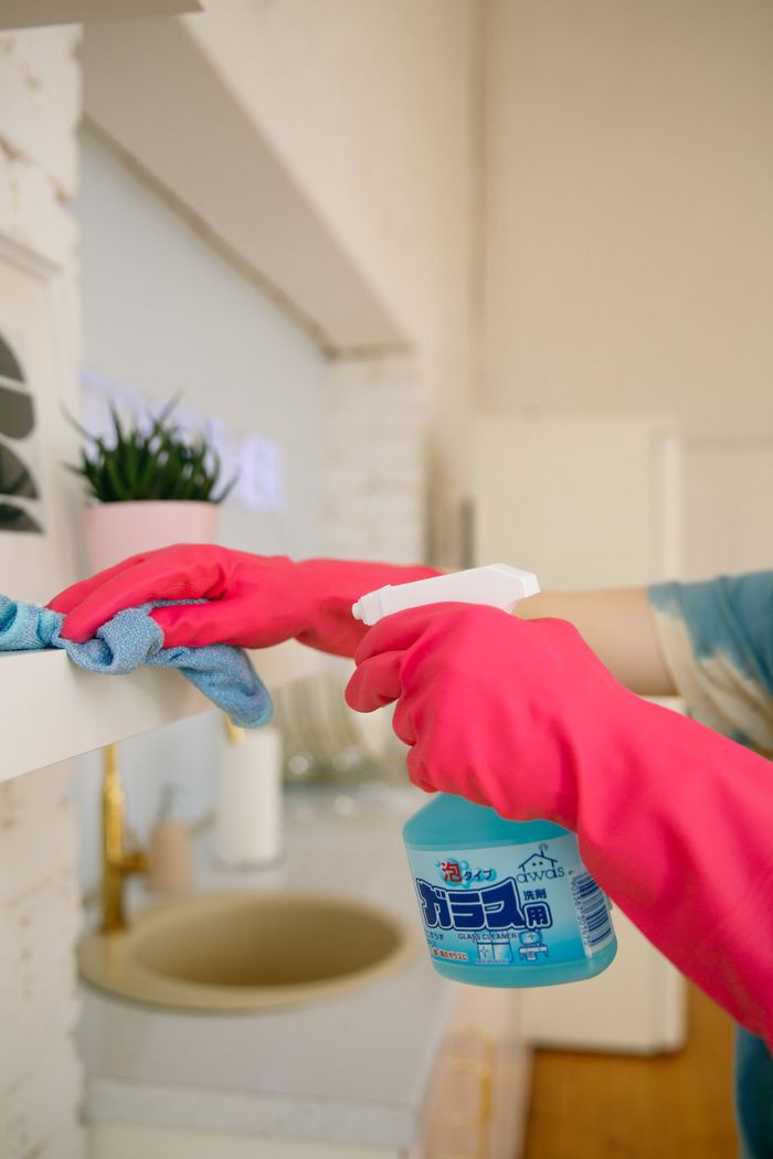 why-choose-us Person using spray bottle and cloth for cleaning a kitchen shelf, ensuring hygiene and cleanliness.